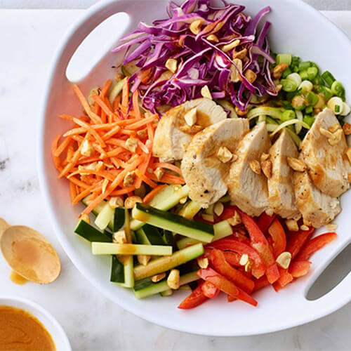 Turkey zucchini thai noodle salad sprinkled with peanuts on a white bowl.