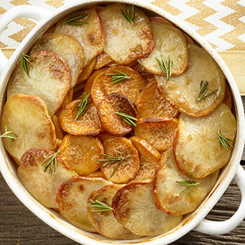 Sweet and russet potatoes, herbed generously and baked a golden brown, served in a white tray on a wooden table.