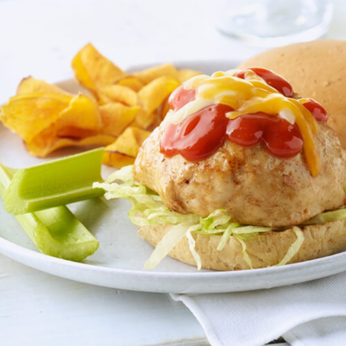 A hearty turkey burger with lettuce, erupting ketchup and cheese with a side of potato chips and celery.