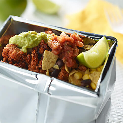 Spicy turkey, salsa, corn, black beans, guacamole, and onion, served in a bag of chips on a white tablecloth.