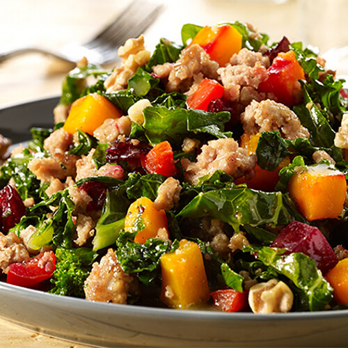 A warm turkey salad made with squash, beets and bell pepper, served on a gray plate atop a wooden table.