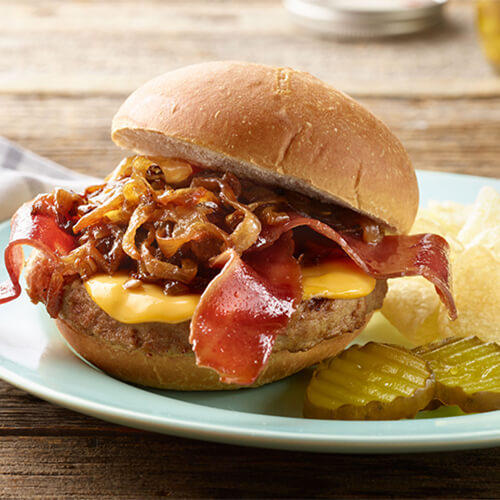 Whiskey bacon turkey burger with a side of pickles on a blue plate.