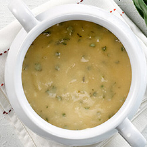 White wine turkey gravy in a white tureen sitting on a white table.