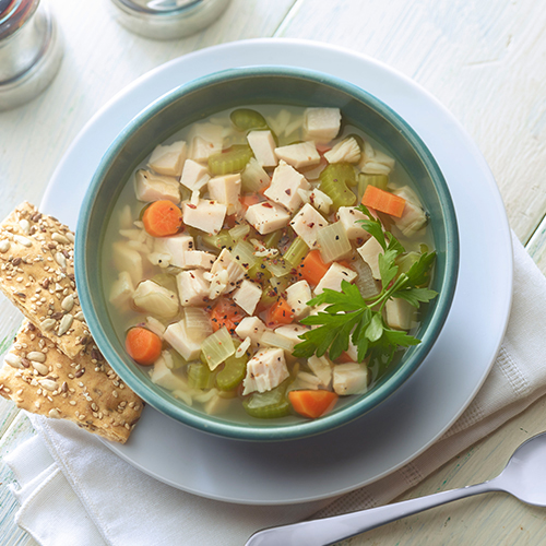 Chopped onions, JENNIE-O® Turkey, carrots, and celery in a chicken broth and a blue bowl.